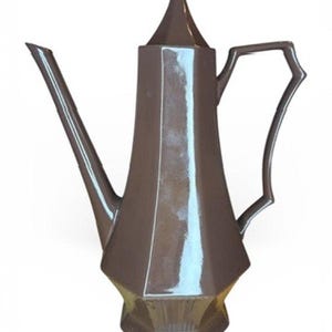 Może przedstawiać: Brązowy ceramiczny dzbanek do kawy z długim dziobkiem i geometrycznym uchwytem. Dzbanek ma wysoki, kanciasty korpus i spiczastą pokrywę. Design jest nowoczesny i elegancki, odpowiedni do serwowania kawy lub herbaty.