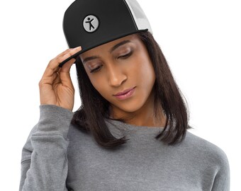 May include: A black and white trucker hat with a white logo of a stick figure in a circle. The hat is being worn by a person with long black hair.