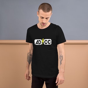May include: Black t-shirt with a white rectangle featuring the text "ADCC" and a yellow lightning bolt.