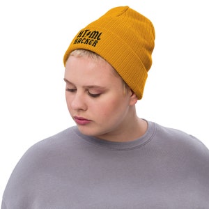 Op de afbeelding: Een mosterdgele beanie met de tekst "HTML HACKER" in het zwart geborduurd op de voorkant.