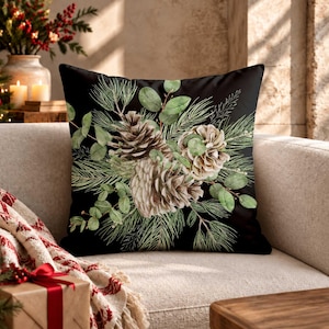 May include: A square throw pillow featuring a black background with a central botanical illustration of brown pinecones, green eucalyptus leaves, and pine needles arranged in a cluster across the front of the fabric cover.