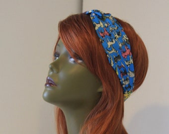 May include: A blue headband with a colorful pattern of animals. The headband is worn on a mannequin with long, red hair.