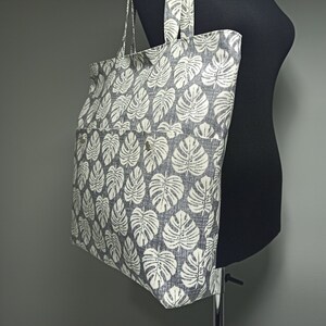 May include: A large grey tote bag with a white leaf print. The bag has a zipped pocket on the front.