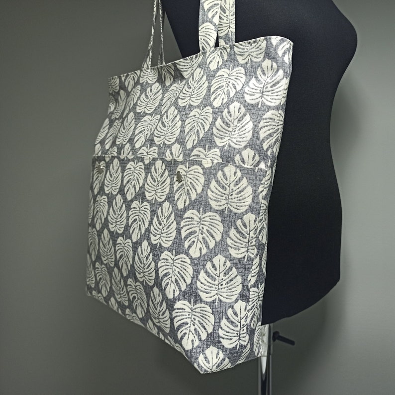 May include: A large grey tote bag with a white leaf print. The bag has a zipped pocket on the front.