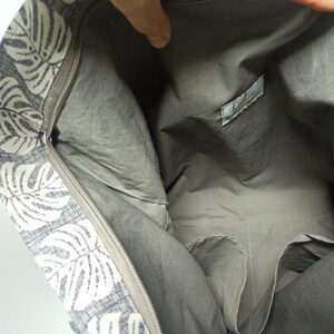 May include: The inside of a grey tote bag with a white and grey floral print. The bag has a zipper closure and a small pocket on the inside.