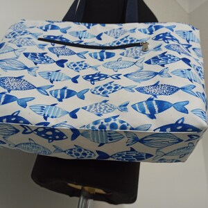 May include: A white canvas tote bag with a blue and white fish pattern. The bag has a zippered pocket on the front.