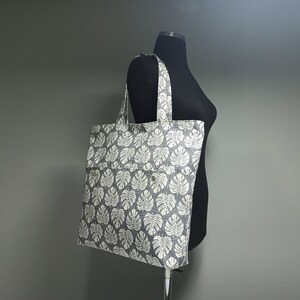 May include: A grey and white tote bag with a leaf pattern. The bag has a large pocket on the front.