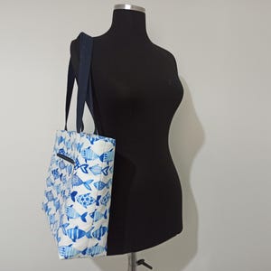 May include: A white tote bag with a blue and white fish pattern. The bag has two navy blue straps.