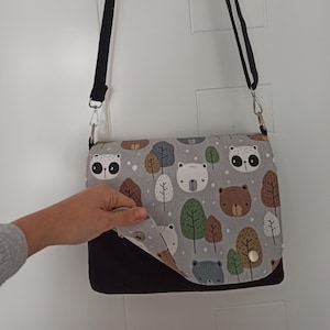 May include: A black and gray shoulder bag with a flap that features a pattern of bears, owls, and trees. The flap is folded down to reveal the black interior of the bag.