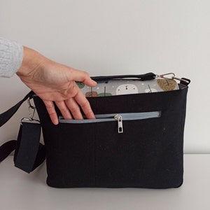 May include: Black canvas shoulder bag with a zippered pocket and a gray and white patterned lining. The bag has a long adjustable strap.