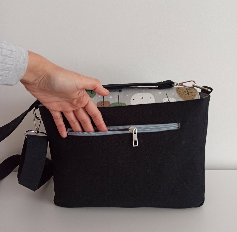 May include: Black canvas shoulder bag with a zippered pocket and a gray and white patterned lining. The bag has a long adjustable strap.