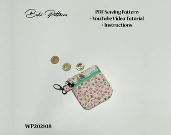 Może przedstawiać: Różowa portmonetka z tkaniny z kwiatowym wzorem i zielonym zamkiem błyskawicznym. Portmonetka ma przymocowany do niej czarny metalowy brelok. Portmonetka leży na białym tle z trzema złotymi monetami.