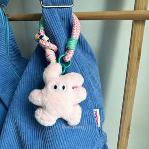 May include: A blue corduroy bag with a pink and green rope handle and a pink plush starfish keychain with googly eyes. The bag has a label that says "tomomi."