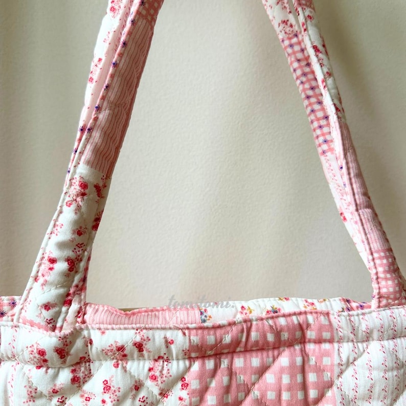 May include: A quilted tote bag with a patchwork design. The bag features a combination of floral, striped, and gingham patterns in shades of pink and white. The handles are made of the same quilted fabric.