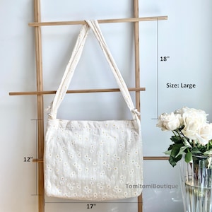 Puede incluir: Una bolsa de lona blanca con estampado de margaritas. La bolsa tiene una correa larga y mide 43 cm de ancho, 30 cm de alto y 46 cm de largo. Talla: Grande.