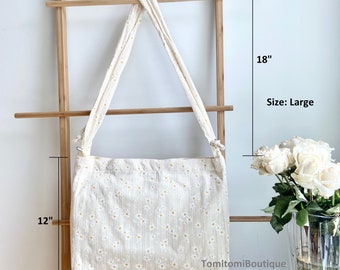 Puede incluir: Una bolsa de lona blanca con estampado de margaritas. La bolsa tiene una correa larga y mide 43 cm de ancho, 30 cm de alto y 46 cm de largo. Talla: Grande.