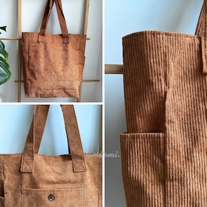 May include: A brown corduroy tote bag featuring a textured ribbed fabric, two sturdy shoulder straps, and external side pockets. The front of the bag includes a pocket secured with a single button. The word tomitomi is printed on the fabric.