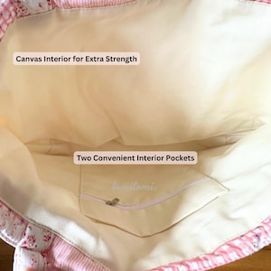 May include: Interior view of a pink and white floral tote bag. The bag features a canvas interior for extra strength and two convenient interior pockets. The bag's interior is a light beige color.