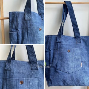 May include: A blue corduroy tote bag featuring a textured ribbed fabric, two sturdy shoulder straps, and a front patch pocket secured with a single brown button. The bag includes a side pocket and a small white label with the text tomitomi.