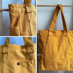 May include: A mustard yellow corduroy tote bag featuring a vertical ribbed texture, two sturdy shoulder straps, and an exterior pocket secured with a single dark brown button. The fabric has a distinct lined pattern throughout the entire surface.