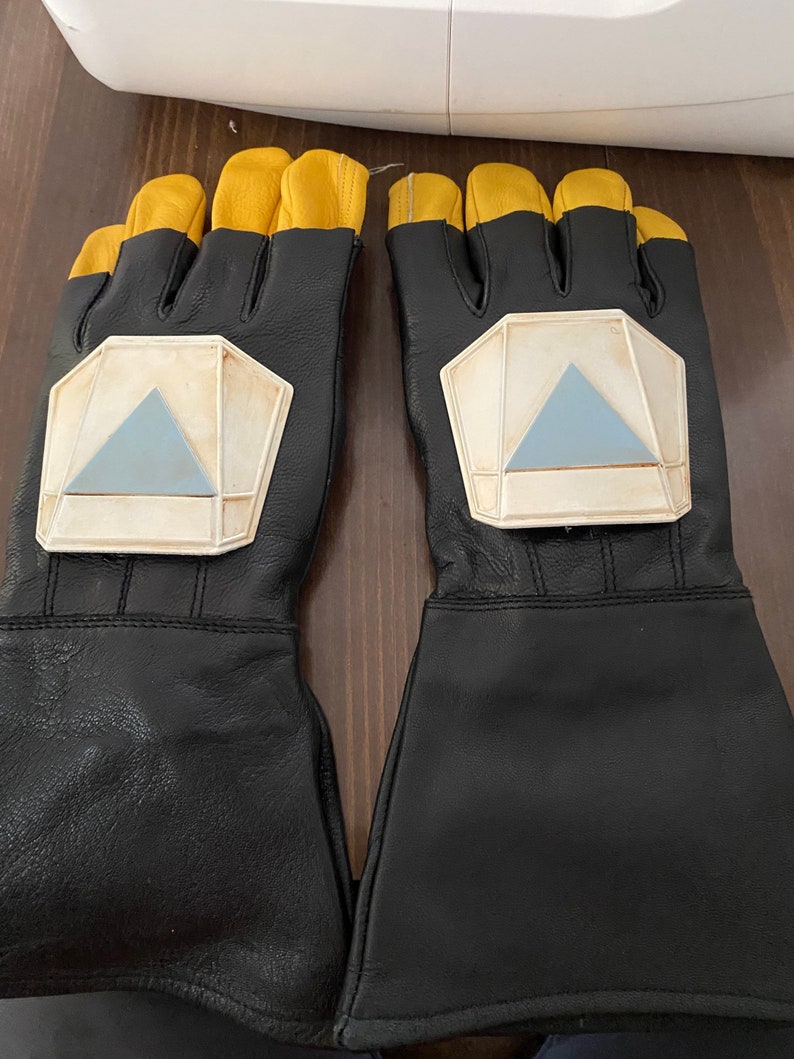 May include: A pair of black leather gloves with yellow accents and a white and blue geometric design on the back of each hand.