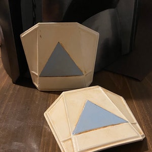May include: Two white ceramic geometric shapes with a blue triangle in the center. The shapes are slightly raised and have a textured surface.