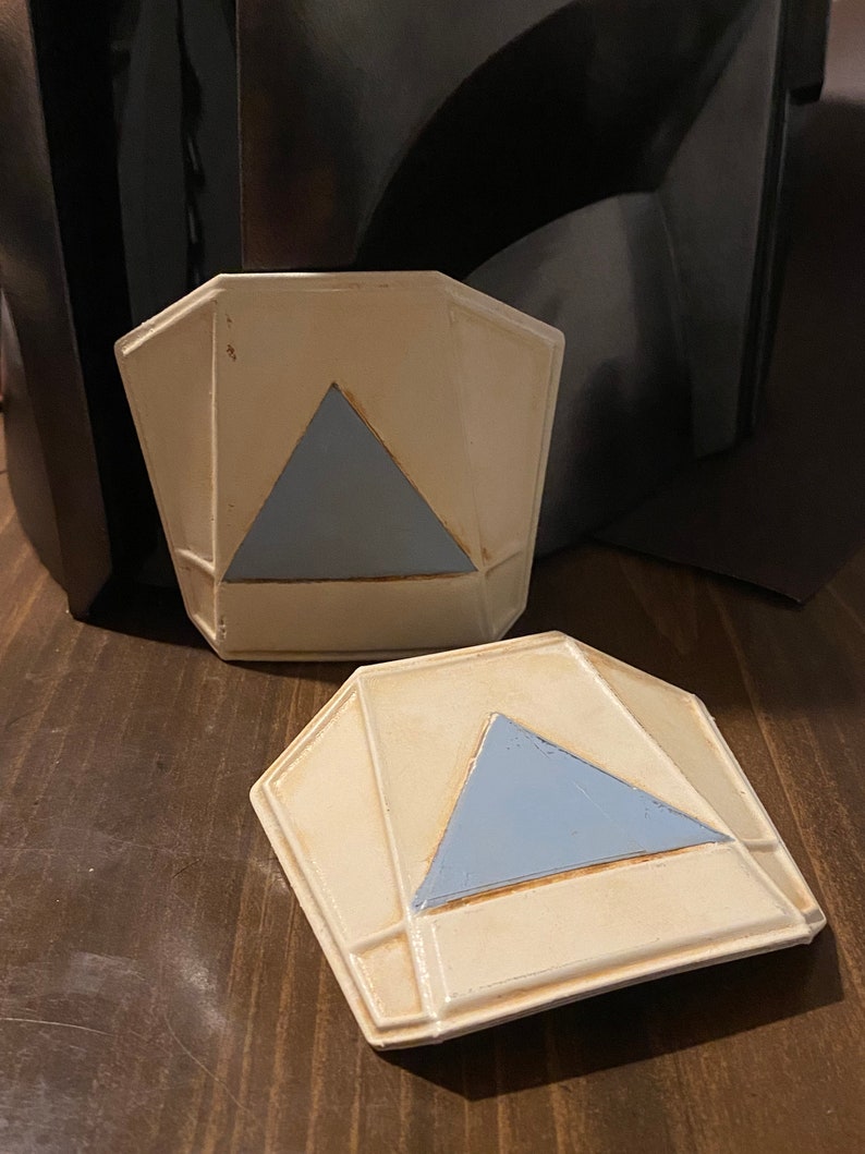 May include: Two white ceramic geometric shapes with a blue triangle in the center. The shapes are slightly raised and have a textured surface.