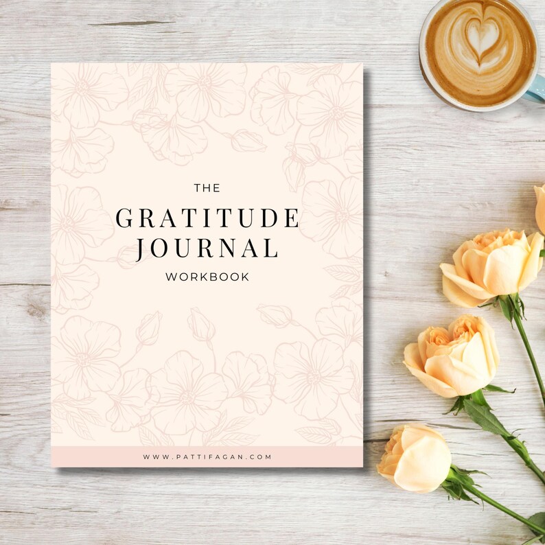 May include: A gratitude journal workbook with a floral design. The cover is a light peach color with the words "The Gratitude Journal Workbook" in black. The website address is at the bottom. A cup of coffee and roses are also in the image.