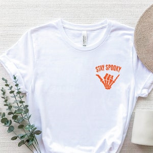 May include: White t-shirt with a graphic of a skeleton hand making a shaka sign and the text "Stay Spooky".