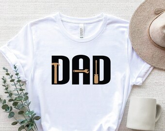 May include: White t-shirt with black text that reads "DAD" with a hammer, wrench, and screwdriver graphic in the middle of the letters.