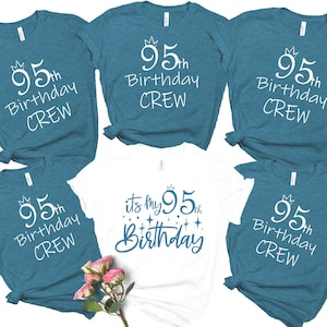 May include: Five short-sleeved t-shirts arranged in a group. Four shirts are heather teal with white text reading 95th Birthday CREW and a small crown icon. One central white shirt features blue text reading it's my 95th Birthday with stars.