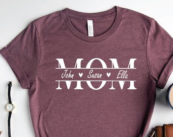 May include: A maroon t-shirt with the word "MOM" in white letters, with the names "John", "Susan", and "Ella" written below, separated by hearts.