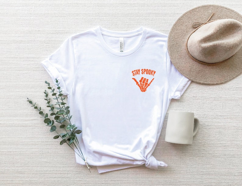 May include: White t-shirt with a graphic of a skeleton hand making a shaka sign and the text "Stay Spooky".