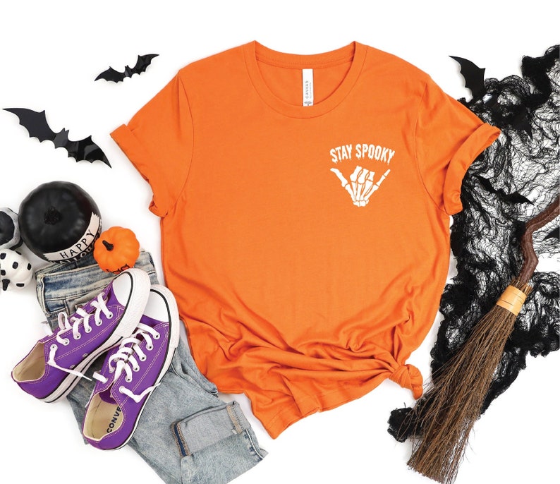 May include: Orange t-shirt with a white skeleton hand making a "hang loose" gesture and the text "Stay Spooky".