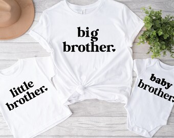 May include: Three white t-shirts with black text. The largest shirt says "big brother." The medium shirt says "little brother." The smallest shirt says "baby brother."