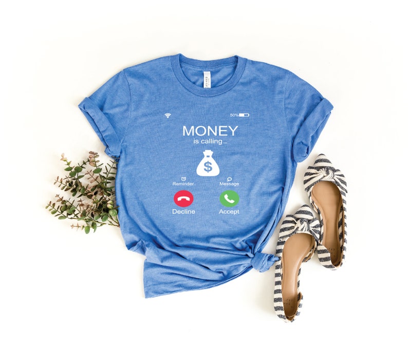 K&ouml;nnte beinhalten: Ein blaues T-Shirt mit einer wei&szlig;en Grafik eines Telefonbildschirms, auf dem "MONEY is calling--" steht, mit einem Geldbeutelsymbol und zwei Kn&ouml;pfen, auf denen "Decline" und "Accept" steht.