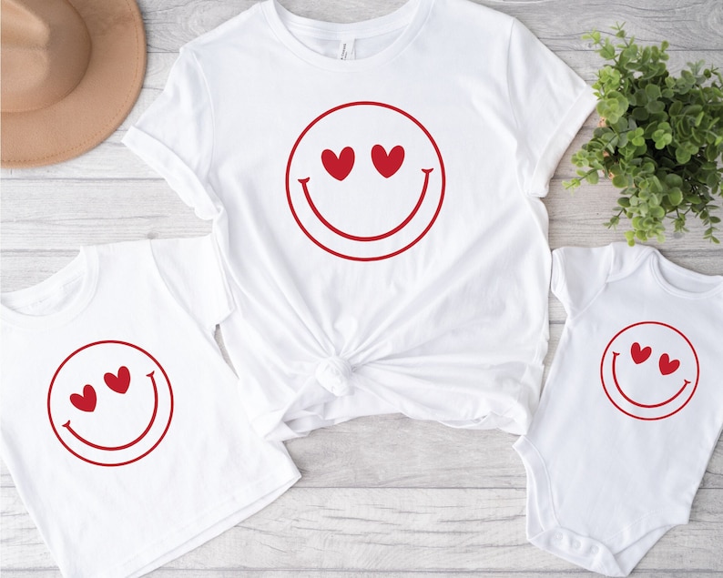 May include: White t-shirts with a red smiley face design. The smiley face has two red hearts for eyes.