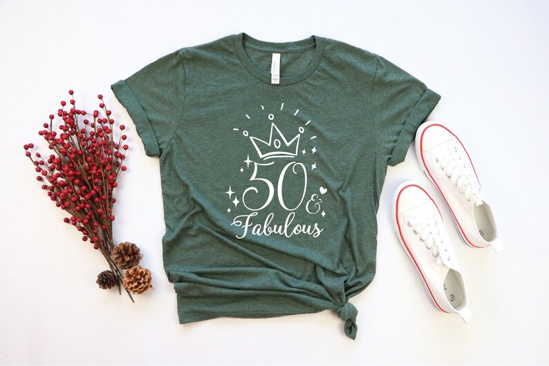 以下が含まれることがあります： 50と王冠が描かれた白いグラフィックが施された緑色のTシャツ。グラフィックには「50 & Fabulous」と書いてあります。