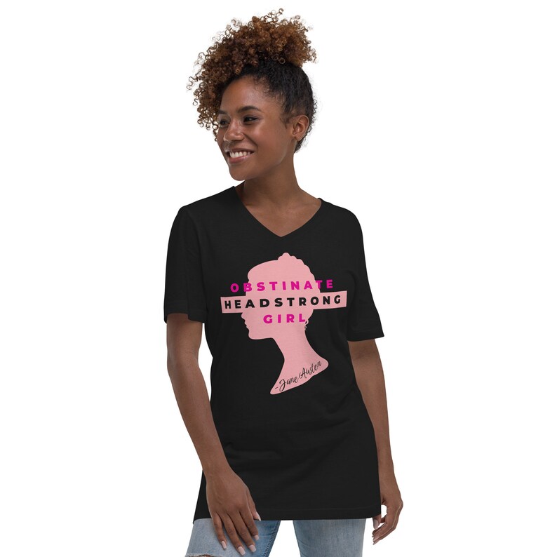 May include: Black v-neck t-shirt featuring a pink silhouette of a woman's head and the text "Obstinate Headstrong Girl" in pink. The text "Jane Austen" is written in smaller font below the silhouette.