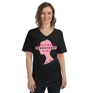 May include: Black v-neck t-shirt featuring a pink silhouette of a woman's head with the text "Obstinate Headstrong Girl" in pink lettering. The text "Jane Austen" is written in smaller pink letters below the silhouette.