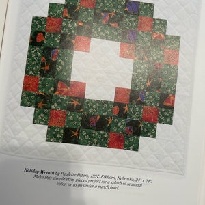 K&ouml;nnte beinhalten: Ein gr&uuml;ner, roter und blauer Patchwork-Decken in Form eines Kranzes. Die Decke besteht aus Quadraten und ist 61 cm x 61 cm gro&szlig;. Der Text "Holiday Wreath by Paulette Peters, 1997, Elkhorn, Nebraska, 24" x 24". Make this simple strip-pieced project for a splash of seasonal color, or to go under a punch bowl." ist unter der Decke gedruckt.