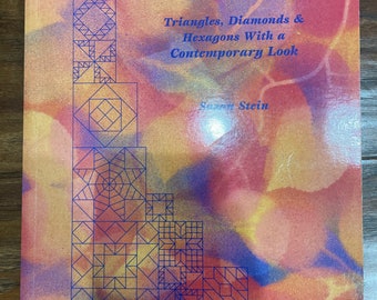 May include: A book titled "Colorful Angles" with text that reads "Triangles, Diamonds & Hexagons With a Contemporary Look." The cover features a geometric design in blue on a colorful background of orange, yellow, and blue.