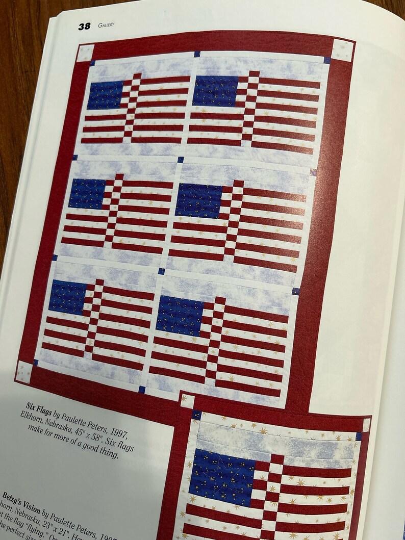 K&ouml;nnte beinhalten: Sechs amerikanische Flaggen sind in einem Quiltmuster zusammengen&auml;ht. Die Flaggen sind rot, wei&szlig; und blau mit wei&szlig;em Hintergrund und goldenen Sternen. Der Quilt ist 45 Zoll mal 58 Zoll gro&szlig;. Der Titel "Six Flags" steht unter dem Quilt.