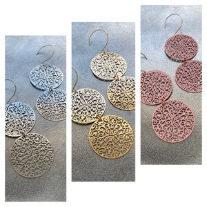 Può includere: Tre paia di orecchini pendenti con un designo a filigrana. Gli orecchini sono disponibili in argento, oro e oro rosa.