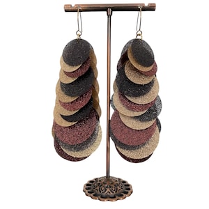 May include: A pair of long dangle earrings with multiple layers of black, gold, and burgundy glitter circles. The earrings are displayed on a metal stand.