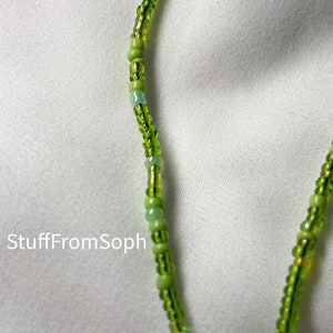 May include: Close-up of a beaded necklace with a variety of green beads. The beads are strung together to create a delicate and intricate design. The necklace is set against a white background. The text "StuffFromSoph" is visible.