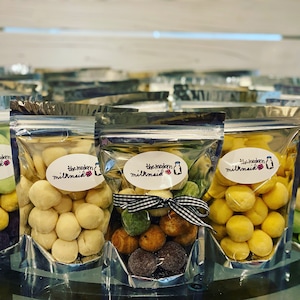May include: A variety of small, round, colorful candies in clear plastic bags with the text "The Modern Milkmaid" on the front. The candies are in different colors, including green, yellow, white, and purple.