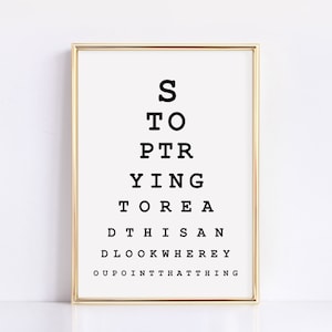 May include: A gold framed print with a black and white eye chart that reads "STOP TRYING TO READ THIS AND LOOK WHERE I POINT THAT THING".