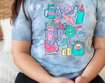 May include: A light blue tie-dye t-shirt with a colorful graphic design of various baby and breastfeeding items. The graphic includes a breast pump, bottles, a bra, a pacifier, a spoon, a water bottle, and the text "Milk maker", "The munchies", "Liquid gold", "Breast please", "Baby powder", "So thirsty", and "H2O".