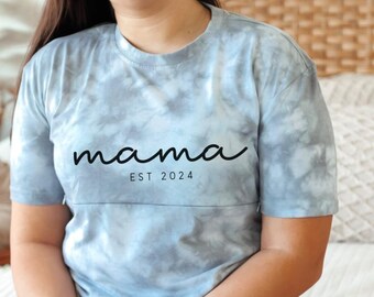 May include: A light blue tie-dye t-shirt with the text "mama est 2024" in black.